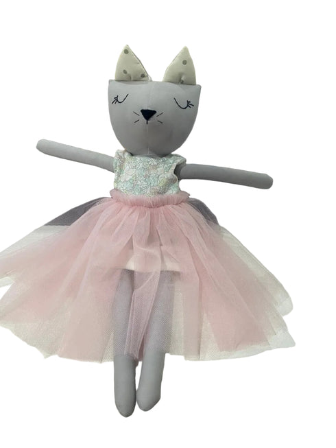 Stuffed toy cat in a pink dress on a white surface with a blurred background