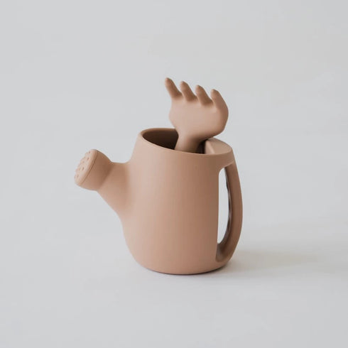 Brown watering can with a unique handle shaped like a hand on a light gray background.