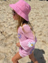 Child in a pink outfit with floral designs on a sandy beach