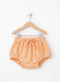 Orange baby bloomers on a wooden hanger against a white background