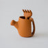 A terracotta-colored silicone watering can with a silicone rake inside, displayed against a white background.